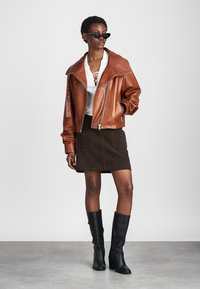 Brun læder bomberjakke med overdimensioneret krave, parret med en hvid snørebåndstop, brun suedes mini-nederdel og sorte knæhøje støvler.