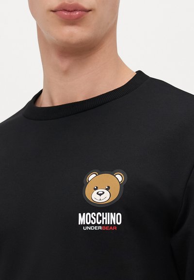 Black sweatshirt featuring a bear graphic in brown, white, and black. Includes "MOSCHINO UNDERBEAR" text in white and red. Ribbed collar.