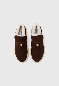 Pantofi slip-on din suede maro închis, cu căptușeală de blană crem și tălpi din cauciuc, având logo-uri aurii "SM" pe curelele superioare.