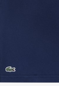 Marineblauw katoenen T-shirt met een subtiele textuur en een klein geborduurd groen krokodillenlogo in de linkeronderhoek.