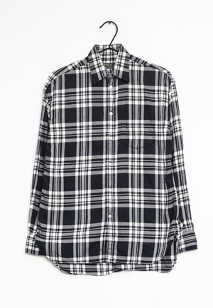 Czarna, biała i szara kraciasta koszula na guziki z długim rękawem, wisząca na czarnym wieszaku na białym tle.