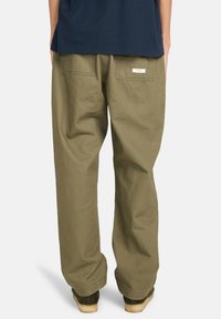 Cargo broek in olijfgroen, gemaakt van dikke katoenen stof. Kenmerkt zich door brede pijpen, twee achterzakken en een label boven de rechterzak.