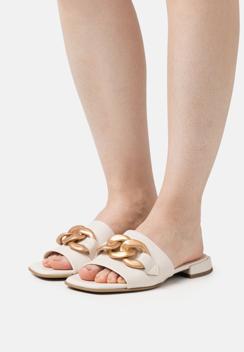 Pieds portant des sandales blanches à bout ouvert avec une grande chaîne dorée décorative sur les brides et des talons blocs bas.