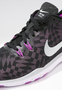 Schwarze und lila Nike Sportschuhe verfügen über ein strukturiertes Mesh-Obermaterial mit geometrischen Mustern, kontrastierenden Schnürsenkeln und einem weißen Swoosh-Logo.