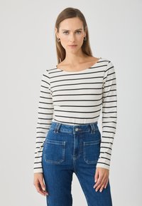 Gestreepte langarmtop in crème met zwarte strepen, gecombineerd met hooggetailleerde blauwe spijkerbroek met voor- en achterzakken.