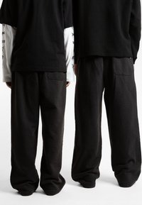 Sorte oversized t-skjorter med lange hvite ermer og mørke vide bukser med baklommer. Stoffet ser mykt og teksturert ut.