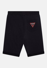 Schwarze Baumwollshorts mit umgeschlagenem Saum, ausgestattet mit einem roten, dreieckigen "GUESS"-Logo-Patch auf der Gesäßtasche. Klassisches, lässiges Design.