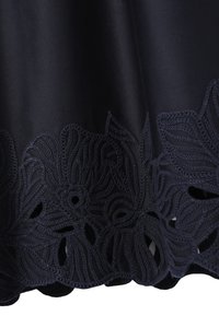 Tissu noir avec une bordure en dentelle florale découpée et brodée le long du bord, montrant des motifs détaillés de fleurs et de feuilles.
