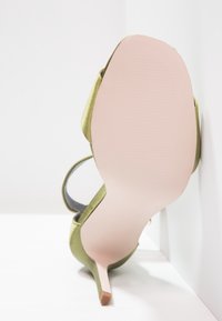 Zelená saténová vysoká bota na podpatku s úzkým stiletto, která má růžovou podrážku a černý pásek. Hladký povrch a minimální zdobení.