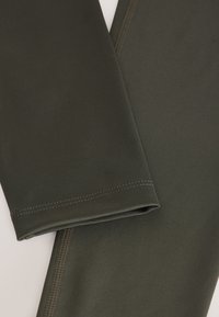 Donkergroene leggings gemaakt van rekbare stof, voorzien van vlakke naden en een gladde textuur. Het ontwerp heeft een nauwsluitende pasvorm.