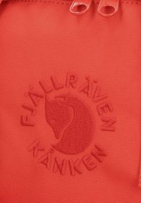 Toppa di tessuto rosso con logo in rilievo e testo "FJÄLLRÄVEN KÅNKEN" e un design stilizzato di una volpe, texture liscia e dettagli di cucitura sottili.