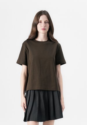 Brown cotton t-shirt with short sleeves and a rounded neckline, layered over a pleated black skirt. Simple, casual design with a relaxed fit.