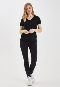 Čierne tričko s výstrihom do V a krátkymi rukávmi v kombinácii s čiernymi slim-fit nohavicami. Biele tenisky s reflexnými detailmi dopĺňajú outfit.