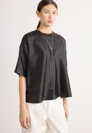 Top preto, de corte solto, feito de material texturizado, com decote redondo e mangas curtas. Apresenta um colar longo de prata como destaque.