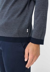 Marineblauwe gebreide trui met een textuurpatroon, voorzien van een geribde mouw- en onderzoom. Klein logo-label zichtbaar aan de zijkant.