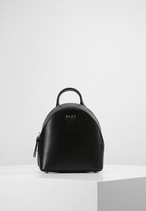 Sort læder mini-rygsæk med øverste håndtag, gyldent lynlås og frontlogo DKNY, vist på hvid piedestal mod ensfarvet baggrund.