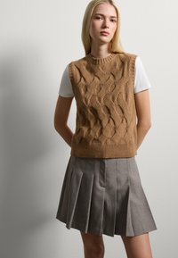 Brown knitted sleeveless sweater with textured wavy pattern, paired with a pleated gray skirt. The outfit features a round neckline.
