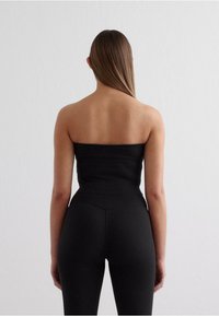 Black strapless top and high-waisted leggings made from a smooth, stretch fabric. The outfit is fitted, emphasizing a sleek silhouette.
