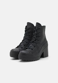 Black high-top boots made of textured leather with laces, featuring a rubber toe cap and thick block heel for added height.