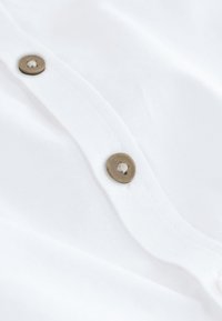 Detail bílého látky se légou se dvěma béžovými knoflíky přišitými bílým nití.
