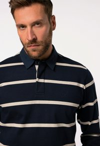 Polo a righe navy e crema con collo, dotato di una patta con tre bottoni e logo ricamato sul lato sinistro del petto.