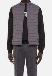 Graue Pufferwesten mit hohem Kragen und Reißverschluss, gestepptem Muster und seitlichen Taschen, getragen über einem schwarzen Sweatshirt.