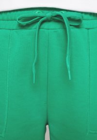 Pantaloni della tuta verdi con vita regolabile tramite cordino, texture a coste e tasche laterali. Il materiale è morbido ed elasticizzato.