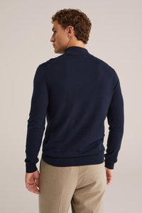 Pullover blu navy a maniche lunghe con colletto e polsini a coste. Texture morbida, design aderente e motivo uniforme. Pantaloni visibili sotto.