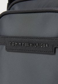 Zaino in tessuto nero con superficie texturizzata, caratterizzato da un pronuncato patch del logo "TOMMY HILFIGER" e cuciture rinforzate.