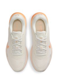 Paire de chaussures de course Nike blanches et pêche vues de dessus, avec une texture en tricot, des semelles en mousse et des lacets noués en nœuds papillon.
