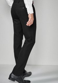 Sorte bukser med slim fit, glat tekstur, baglomme med knaplukning, båret med sorte dress sko og mønstrede sokker.