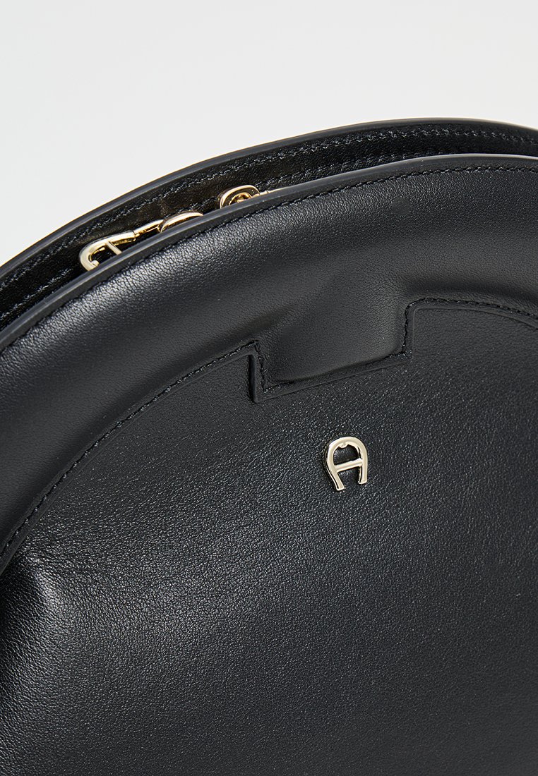 Schwarze Leder-Handtasche in runder Form mit glatter Textur, ausgestattet mit einem goldenen Reißverschluss und einem kleinen goldenen Logo-Akzent.