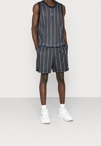 Débardeur de sport noir et shorts avec des rayures verticales blanches et une texture en maille ; comporte un petit logo sur la poitrine ; associé à des baskets blanches.