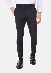 Pantaloni eleganti neri con una vestibilità slim, dotati di tasche laterali e tessuto testurizzato, abbinati a moccasini neri e una camicia bianca.