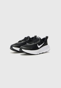 Baskets de sport noires avec un dessus texturé, semelle intermédiaire blanche et semelle extérieure noire. Elles comprennent des lacets et un logo visible sur le côté.