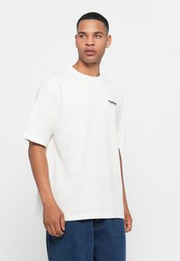 Witte katoenen t-shirt met korte mouwen, ronde halslijn en een klein zwart logo op de linkerborst. Losse pasvorm en een soepele textuur.