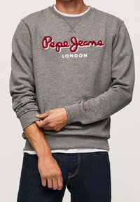 Felpa grigia con collo rotondo e maniche lunghe. "Pepe Jeans" ricamato in rosso sopra "LONDON" in bianco. Polsini e orlo a costine.