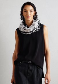 Top senza maniche nero abbinato a una gonna di jeans nera. L'outfit è accentuato da una sciarpa a motivi grigio chiaro e nera avvolta attorno al collo.