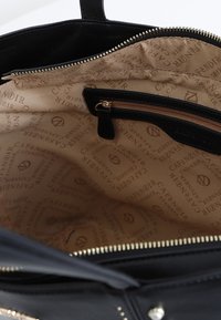 Interno di una borsa a mano in pelle nera con fodera in tessuto beige caratterizzata da un motivo con logo ripetuto. Include una tasca con zip e dettagli in oro.
