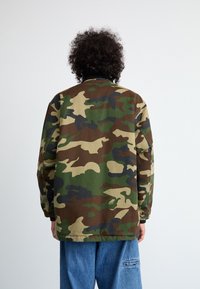 Μπουφάν καμουφλάζ με μίγμα πράσινων, καφέ και μαύρων σχεδίων, σε χαλαρή εφαρμογή και από μαλακό, υφαντό ύφασμα.