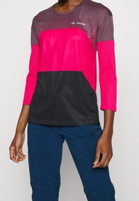 Fuchsia och svart långärmad träningsskjorta gjord av lätt och andningsbart tyg, med rundad halsringning och texturerade accenter.