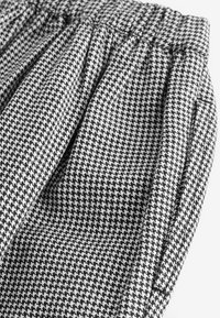Materiał w czarno-białą kratę houndstooth z plisowaną fakturą i elastycznym paskiem w talii, prezentujący utkany wygląd i gładkie wykończenie.