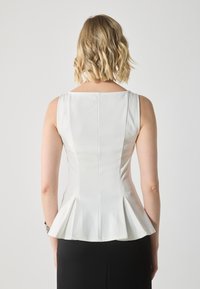 Vit peplumtop med ärmlös design, slät textur och fyrkantig halsringning. Har en söm i mitten och utställd nederkant.