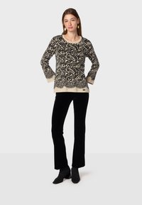 Pull en noir et crème à motif avec un col rond, des manches longues et un ourlet décoratif ; associé à un pantalon en velours noir évasé et des bottines.