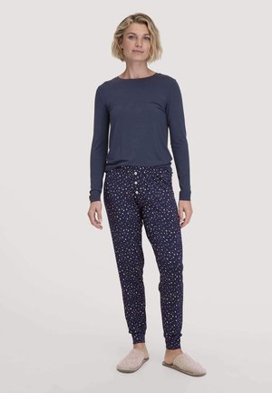 Marineblaues Langarmoberteil kombiniert mit marineblauen Jogginghosen mit gedrucktem Sternenmuster und Knopfakzenten, ergänzt durch helle Slipper.