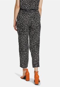 Czarne spodnie w białe kropki, luźny krój, skrócona długość, elastyczny pasek, zestawione z pomarańczowymi sandałami na słupku.