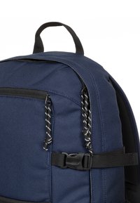 Mochila azul marino hecha de tela resistente, que cuenta con un bolsillo con cremallera, una correa negra con hebilla y cordones trenzados para tirar.