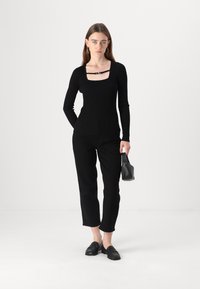 Zwarte geribbelde top met lange mouwen, een vierkante halslijn en banddetail, gecombineerd met zwarte rechte broek en zwarte instappers.