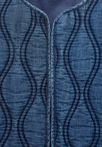 Jeans tkanina z teksturiranim vzorcem, ki ima valovite šive. Bogata modra barva z kontrastnimi temnimi niti in subtilnim sijajem.