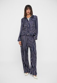 Blusa a righe blu navy con due tasche frontali e orlo arricciato, abbinata a pantaloni larghi coordinati con tasche cargo laterali.